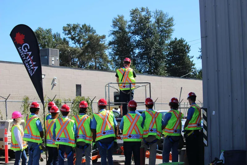 Class watching a boom lift demonstration beside a GAMA SAFETY CANADA flag