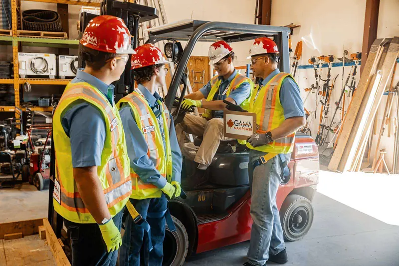 Instructor with a clipboard assessing a forklift trainee while classmates look on