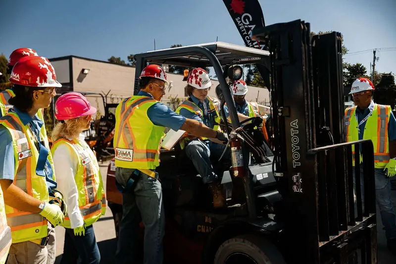 Gama Safety instructor in a forklift cab briefing trainees in hard hats and safety vests
