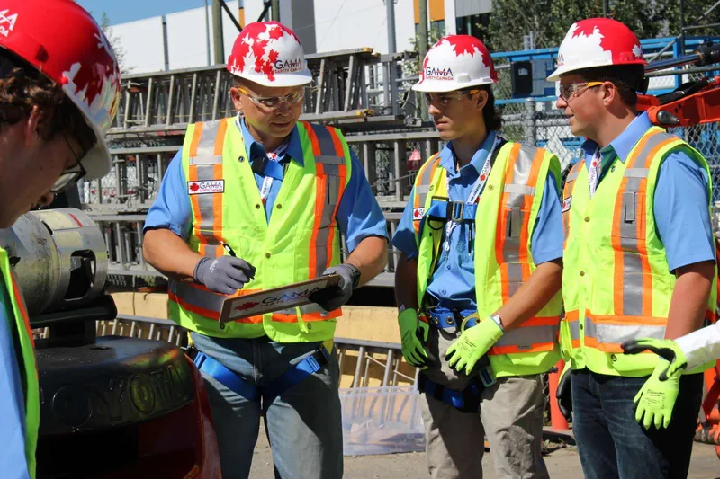 Instructor with a Gama clipboard briefing two trainees in hard hats, vests and gloves