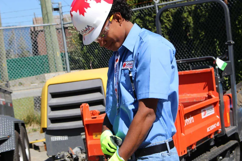 Trainee in a hard hat and safety glasses pulling on high-visibility work gloves