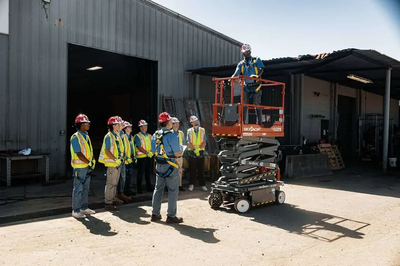 Trainee in a harness demonstrating a scissor lift platform while the class watches